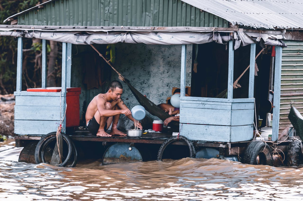 services-04 A man sits on a flooded wooden houseboat during a heavy flood.