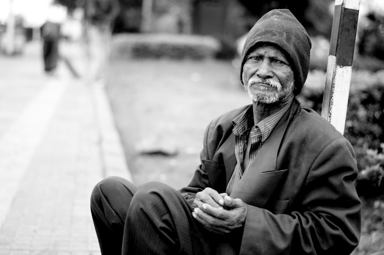 about-us A black and white portrait of an elderly man sitting on the streets, expressing hardship and resilience.